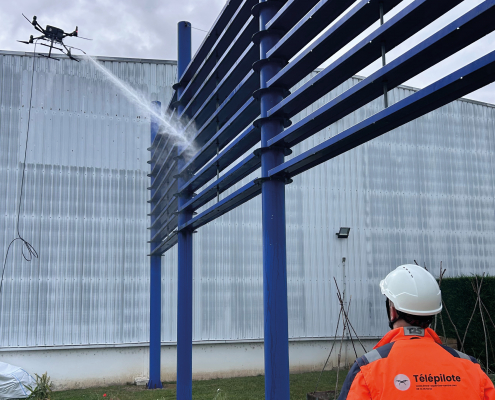 Démoussage par drone de façade avec pulvérisation d'un traitement nettoyant sur un bâtiment industriel en hauteur