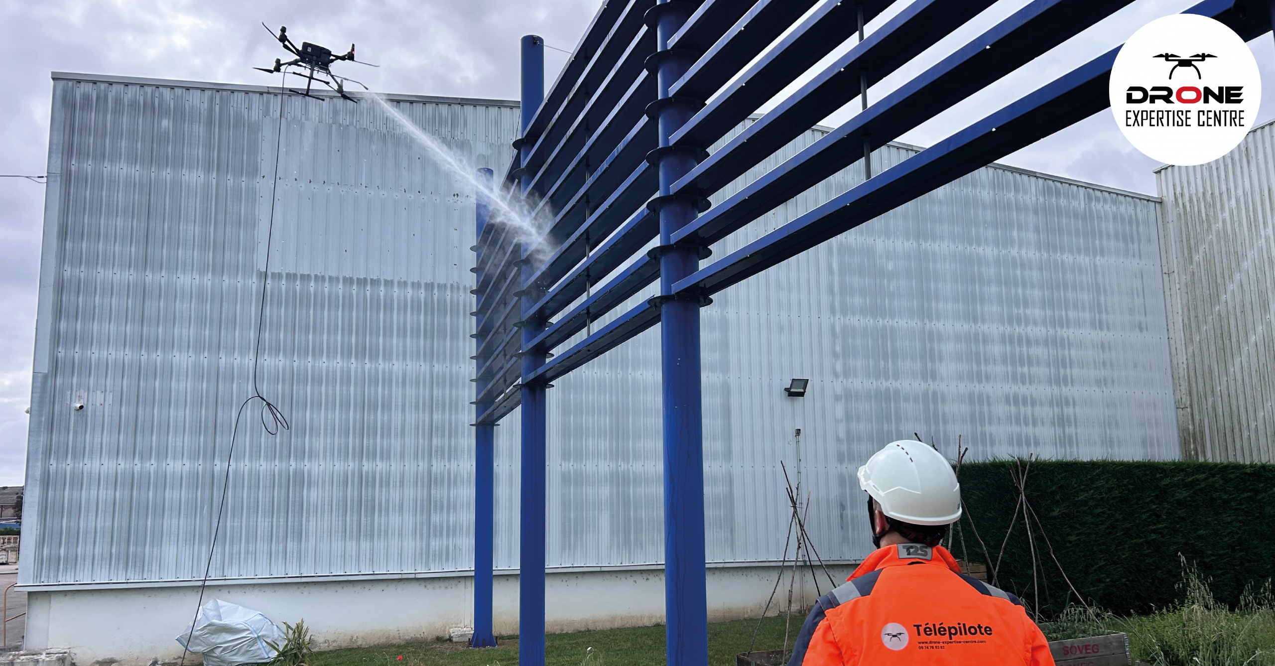 Démoussage par drone de façade avec pulvérisation d'un traitement nettoyant sur un bâtiment industriel en hauteur